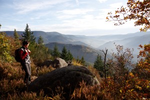 Eine Wanderern steht vor einem Felsen im Naturpark Schwarzwal Mitte-Nord und genießt den Herbstausblick über die Schwarzwaldberge 