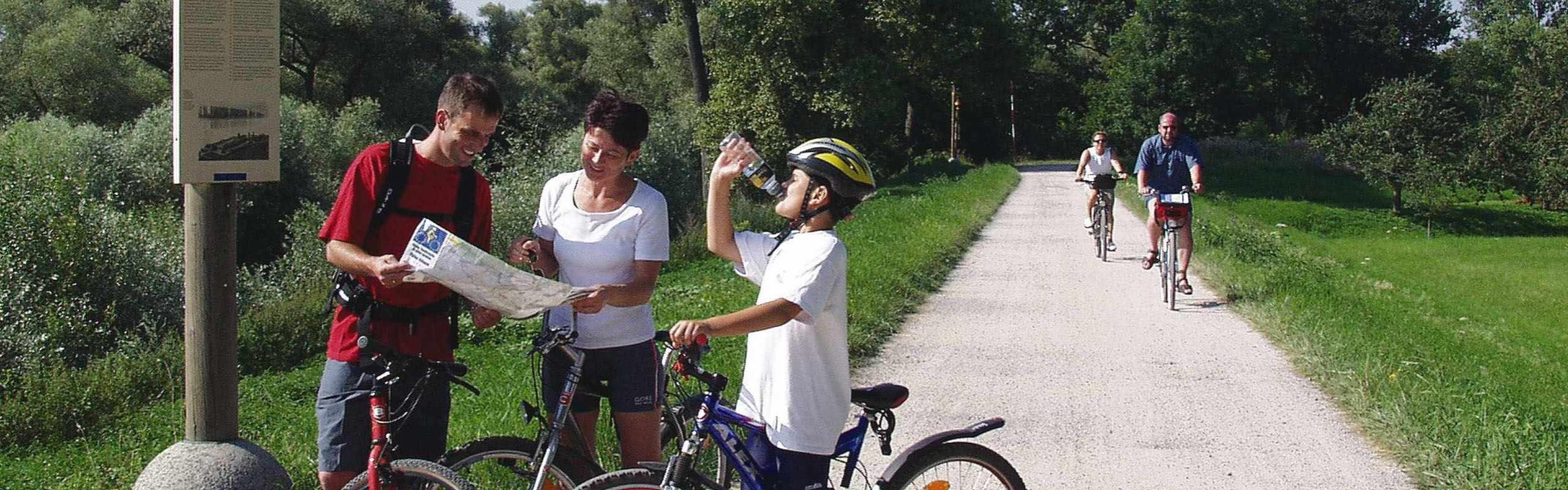 Familie macht eine Radpause vor einer Tafel des PAMINA-Rheinparks und schauen sich eine Karte an bzw trinken etwas