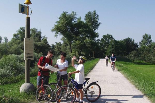 Drei Fahrradfahrer halten vor dem Schild des PAMINA Rheinauenradweg