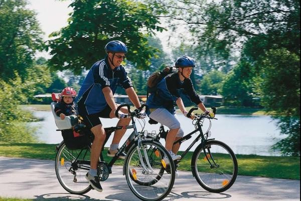 Eltern machen mit Kleinkind im Fahrradsitz eine Radtour am Rhein