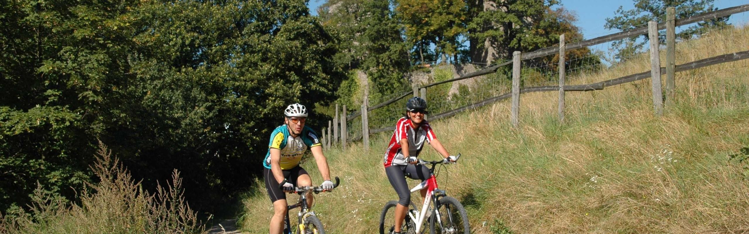 Zwei Mountainbiker mit der Burgruine Altwindeck im Hintergrund 