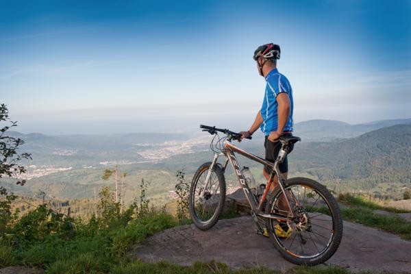 Mann mit Mountainbike genießt von einem Felsen den Ausblick in die Rheinebene