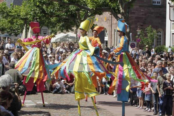 Vier Theaterkünstler aus Stelzen mit bunten Kostümen bei einer Straßenaufführung mit vielen Zuschauern