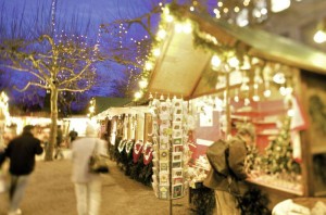 Das Bild zeigt Besucher eines Weihnachtsmarktes mit geschmückten und beleuchteten Weihnachtsmarktbuden
