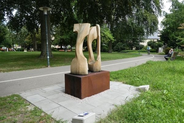 Das Foto zeigt eine Skulptur aus Holz auf einem braunen Rechteck an einer Straße