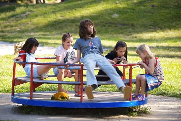 Das Bild zeigt fünf Kinder auf einer Drehscheibe auf einem Spielplatz