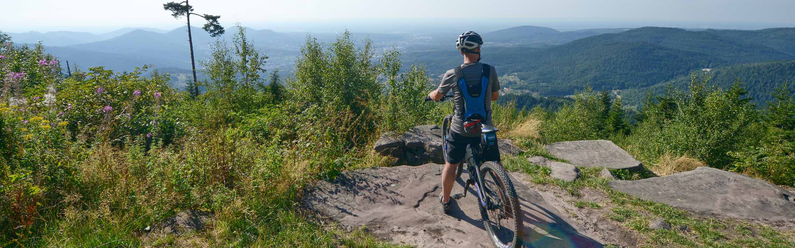 Mountainbiker betrachtet von einer Anhöhe die Landschaft des Schwarzwaldes mit seinen zahlreichen Schwarzwaldbergen