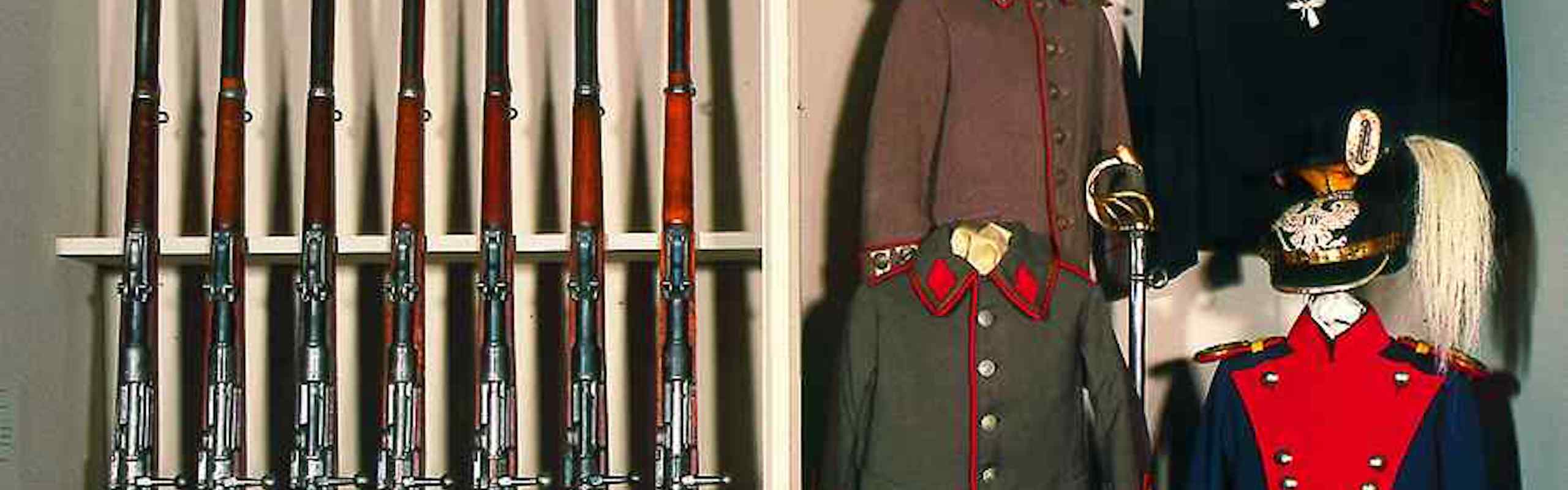 Das Bild zeigt alte ausgestellte Uniformen und Gewehre in einem Museums-Regal